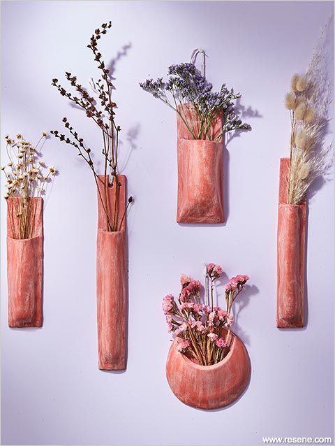 four vases with dried flowers in them on a white wall, one is pink and the other is orange