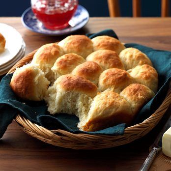 a basket filled with rolls sitting on top of a wooden table next to plates and silverware