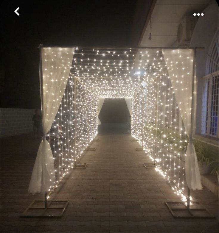 a tunnel with lights on the sides and white curtains over it, in front of a building