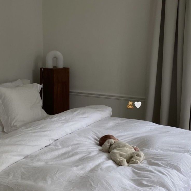 a baby laying on top of a white bed in a bedroom next to a window