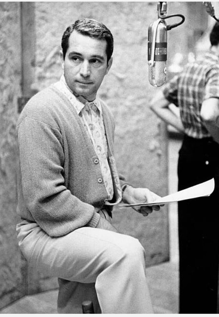 a black and white photo of a man sitting on a stool in front of a microphone