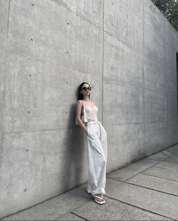 a woman leaning against a wall with her hands on her hips, wearing sunglasses and a white dress