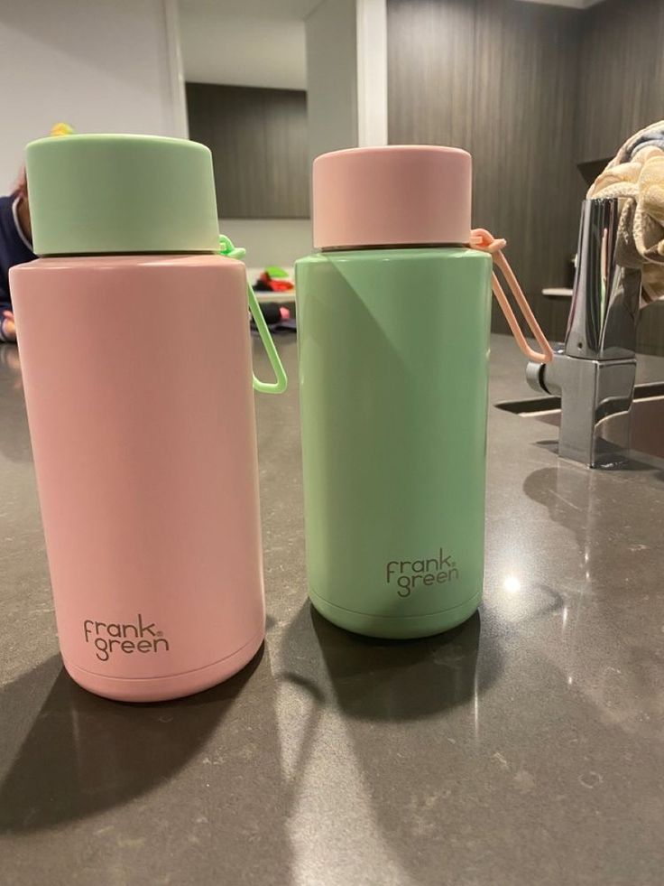 two pink and green insulated water bottles sitting on a counter