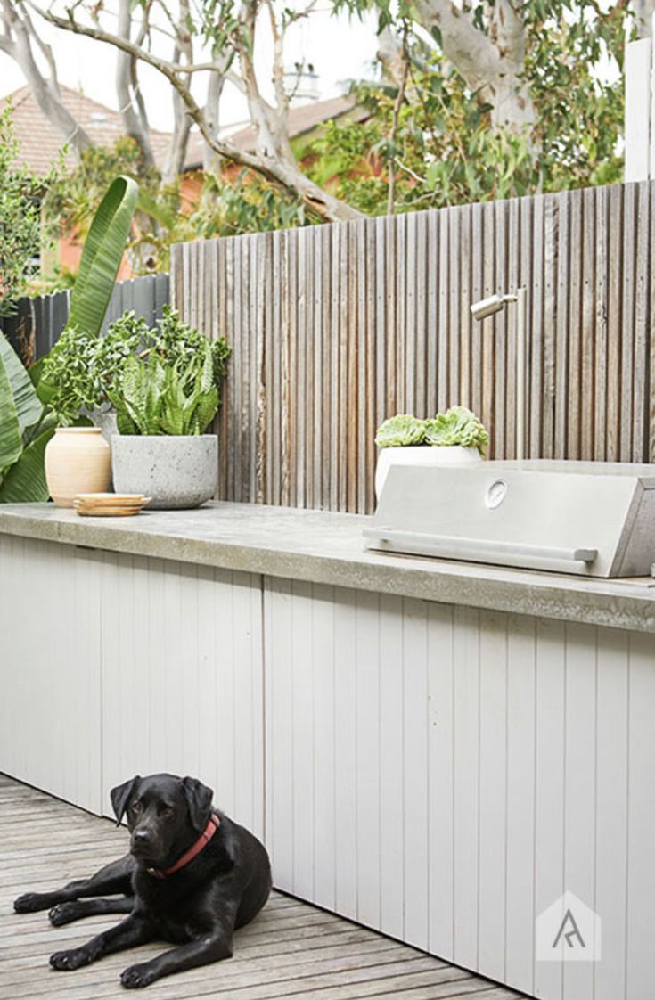 a black dog laying on top of a wooden deck next to a sink and grill