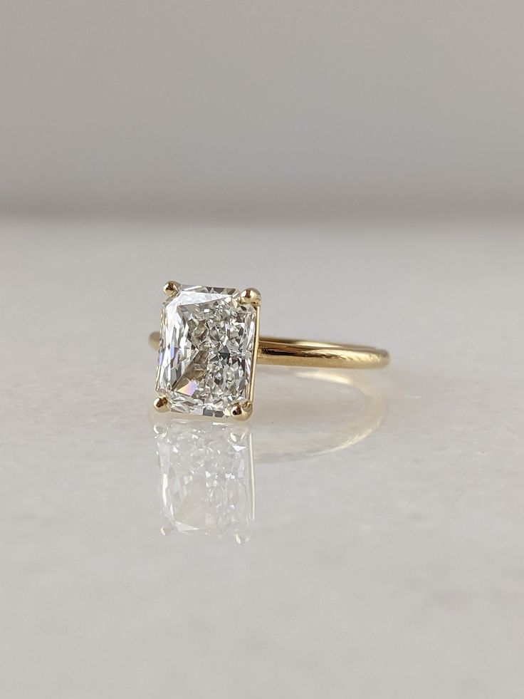 an engagement ring with a square cut diamond in the center, sitting on a white surface