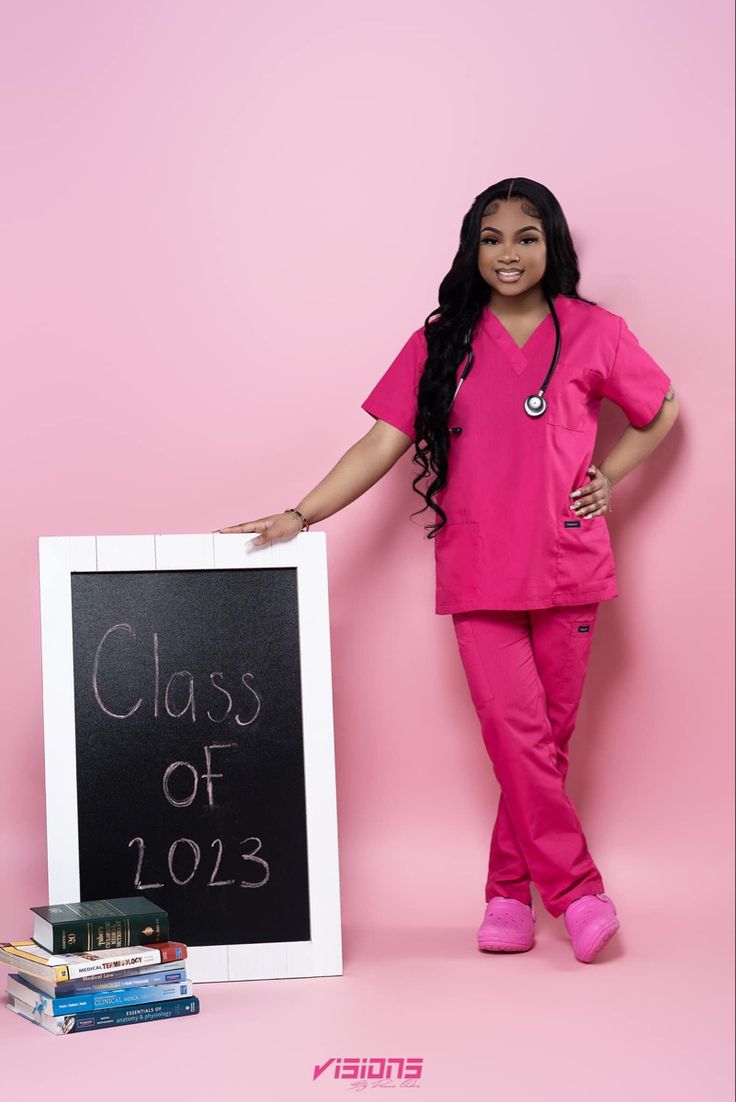 a woman in pink scrubs standing next to a chalkboard with the words class of 2013 written on it