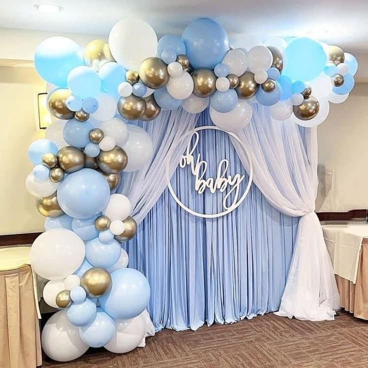 balloons and streamers decorate the backdrop for a baby's first birthday party in blue, gold and white