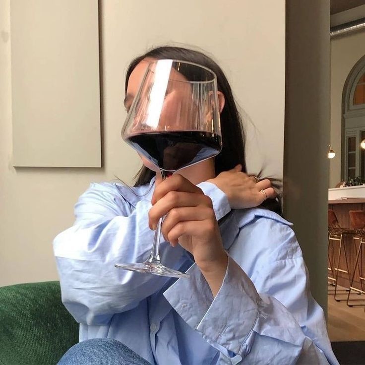 a woman sitting on a couch holding a glass of wine in front of her face