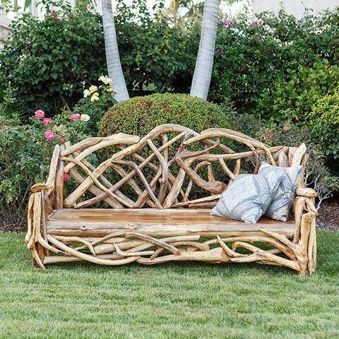 a wooden bench made out of branches in the middle of some flowers and grass with trees in the background