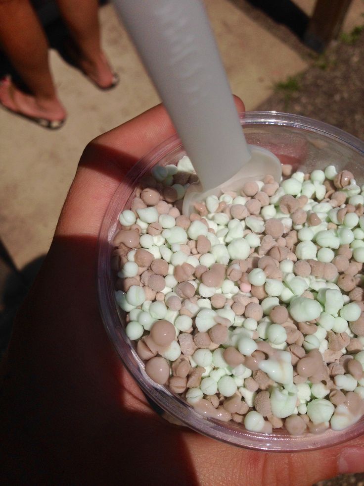 a hand holding a container filled with white and pink marshmallows next to a person's foot