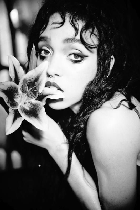 black and white photograph of a woman holding a flower in front of her face with one hand