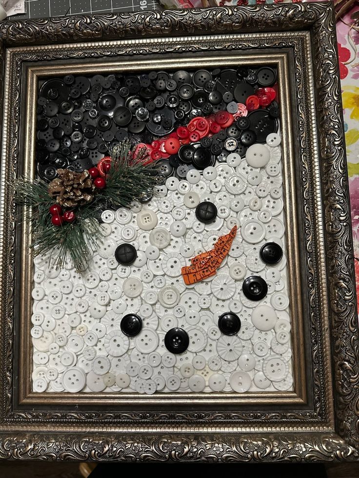 a snowman made out of buttons is displayed in a frame on a table top