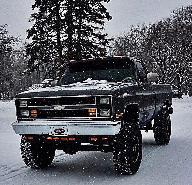 a black truck driving down a snow covered road