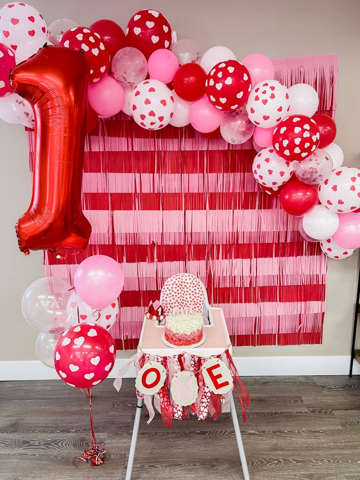 a red and white birthday party with balloons, streamers and cake on a chair