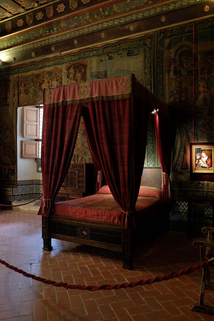 a bedroom with a red canopy bed and paintings on the walls, along with brick flooring