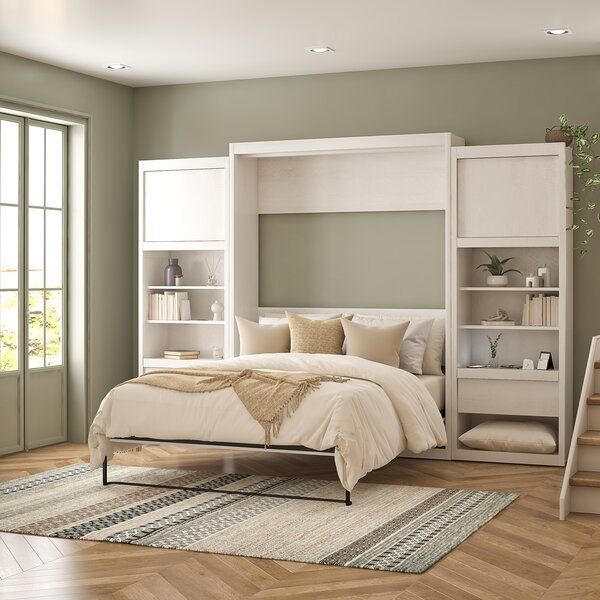 a white bed sitting on top of a wooden floor next to a book shelf filled with books