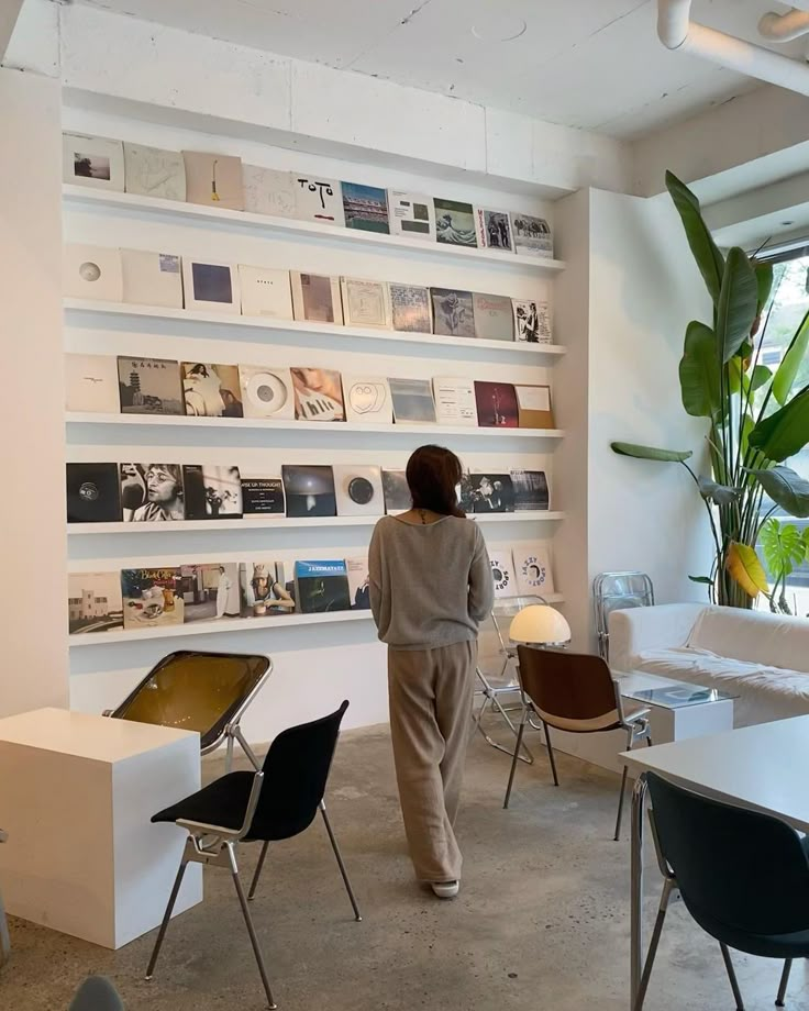 a woman standing in front of a white wall filled with pictures and books on it