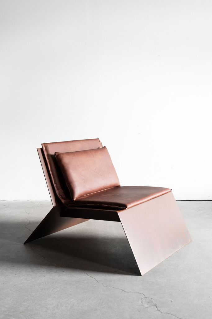 a brown leather lounge chair sitting on top of a cement floor next to a white wall