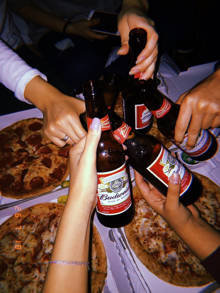 several people are reaching for beer bottles in a circle on top of some pizzas