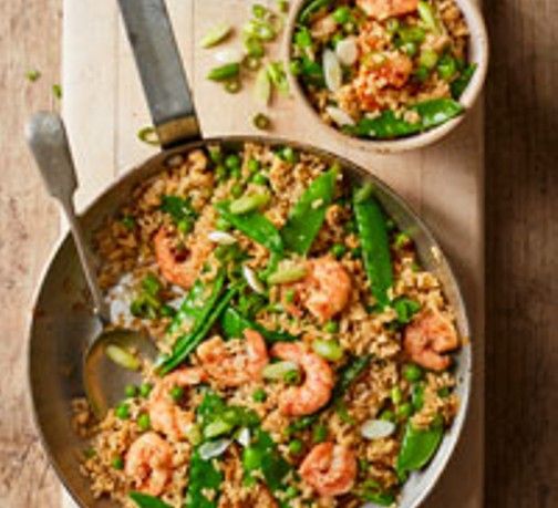 two bowls filled with shrimp and rice on top of a wooden table next to a spoon