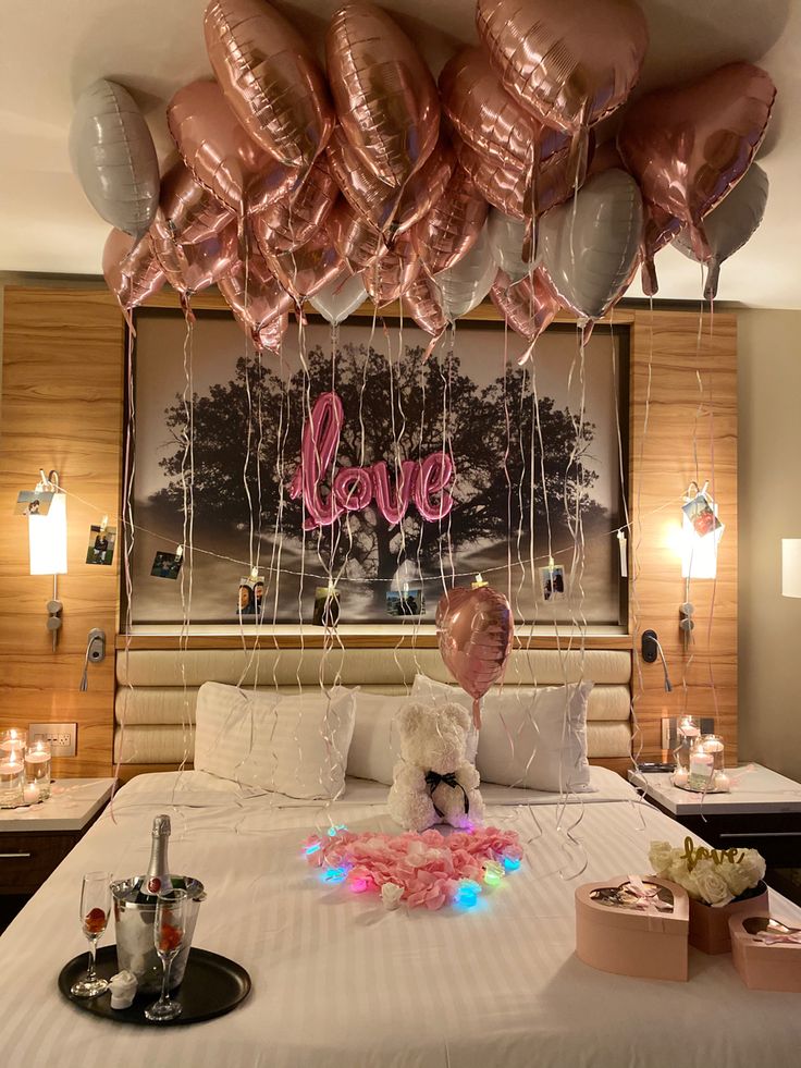 a bed topped with lots of pink and silver balloons hanging from the ceiling above it