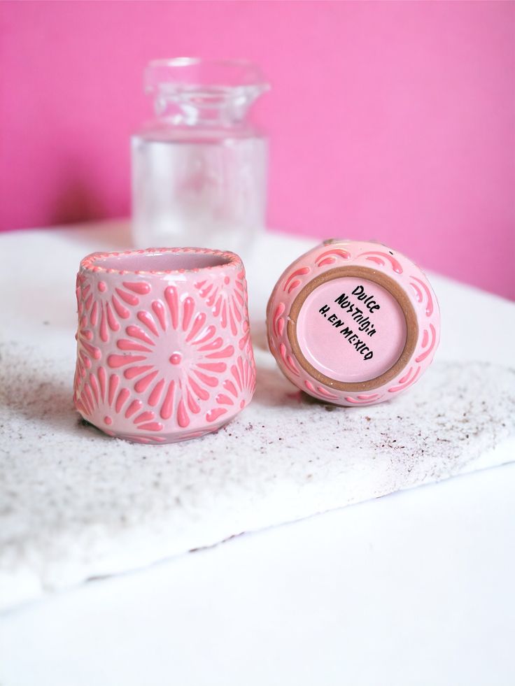 two pink candles sitting next to each other on a white tablecloth with a bottle in the background