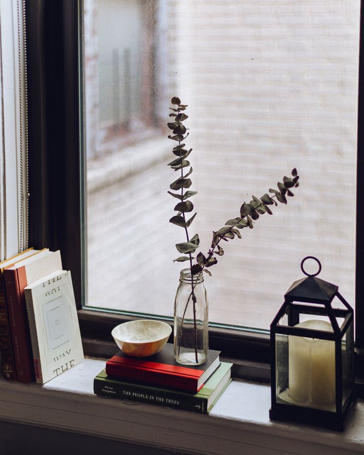 a window sill filled with books and a vase full of flowers next to a candle