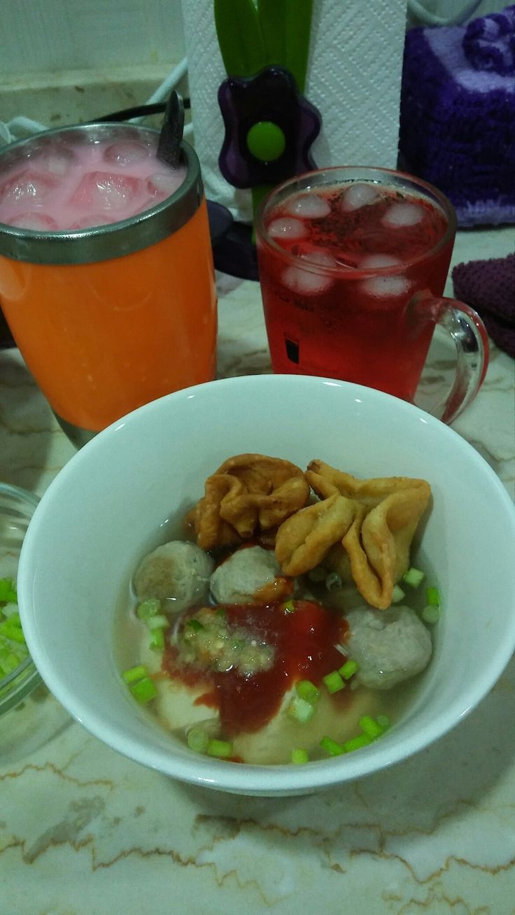 a white bowl filled with food on top of a table next to two glasses of juice