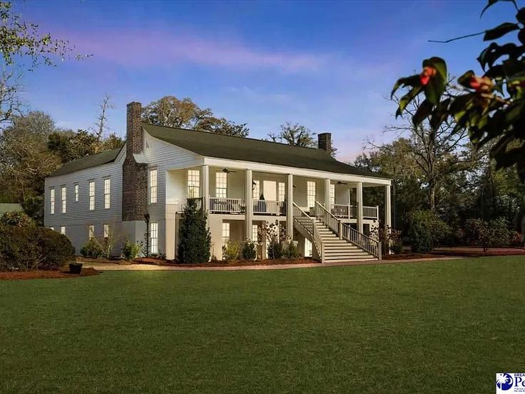 a large white house sitting in the middle of a lush green field with stairs leading up to it