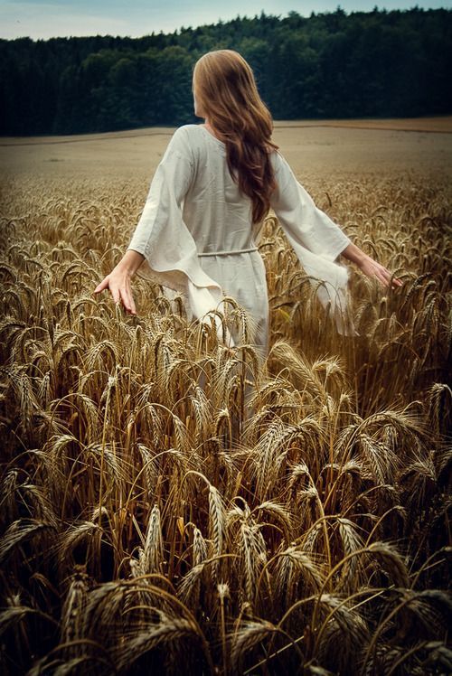 a woman standing in a wheat field with her arms spread out and looking at the sky