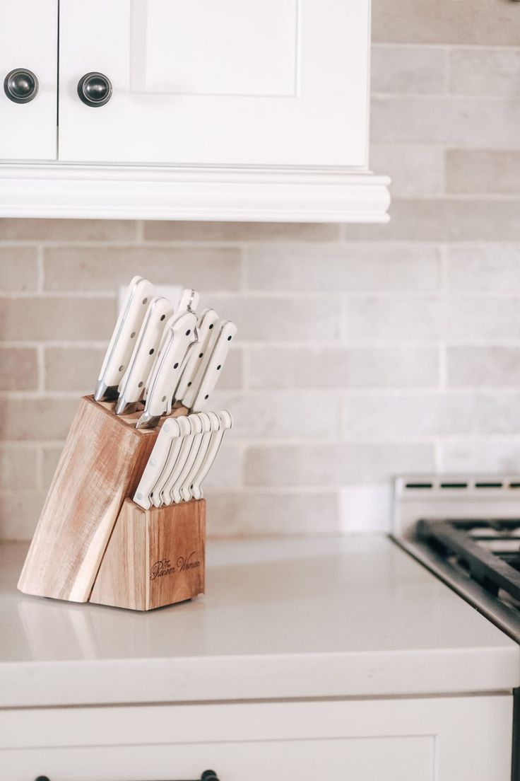 there are many knives in the block on the kitchen counter next to the stove top