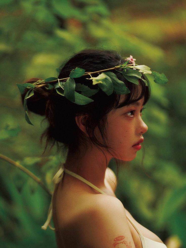 a young woman wearing a leafy headpiece in the woods, looking off into the distance