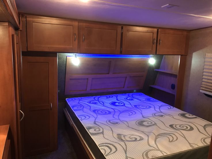 a bed in a room with wooden cabinets and blue lights on the headboard is lit up