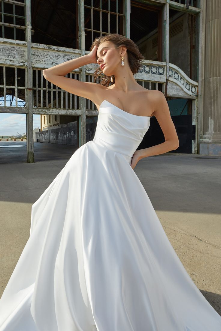 a woman in a white wedding dress posing for the camera with her hand on her head