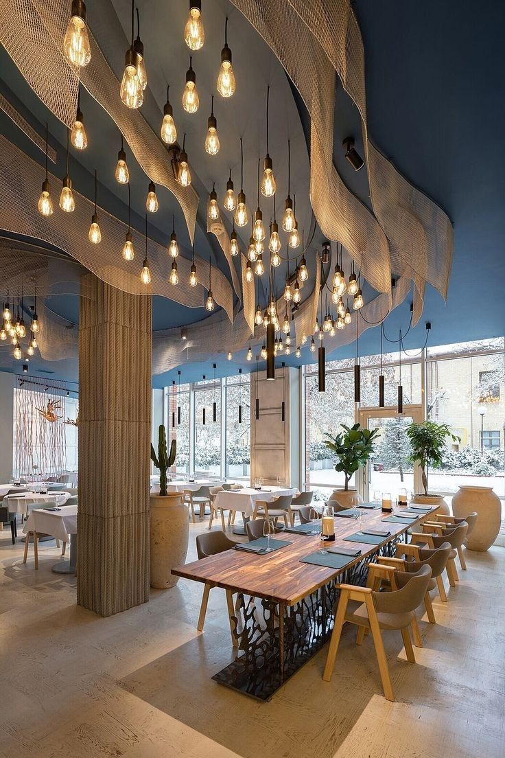 an empty restaurant with wooden tables and chairs, hanging lights over the dining room table