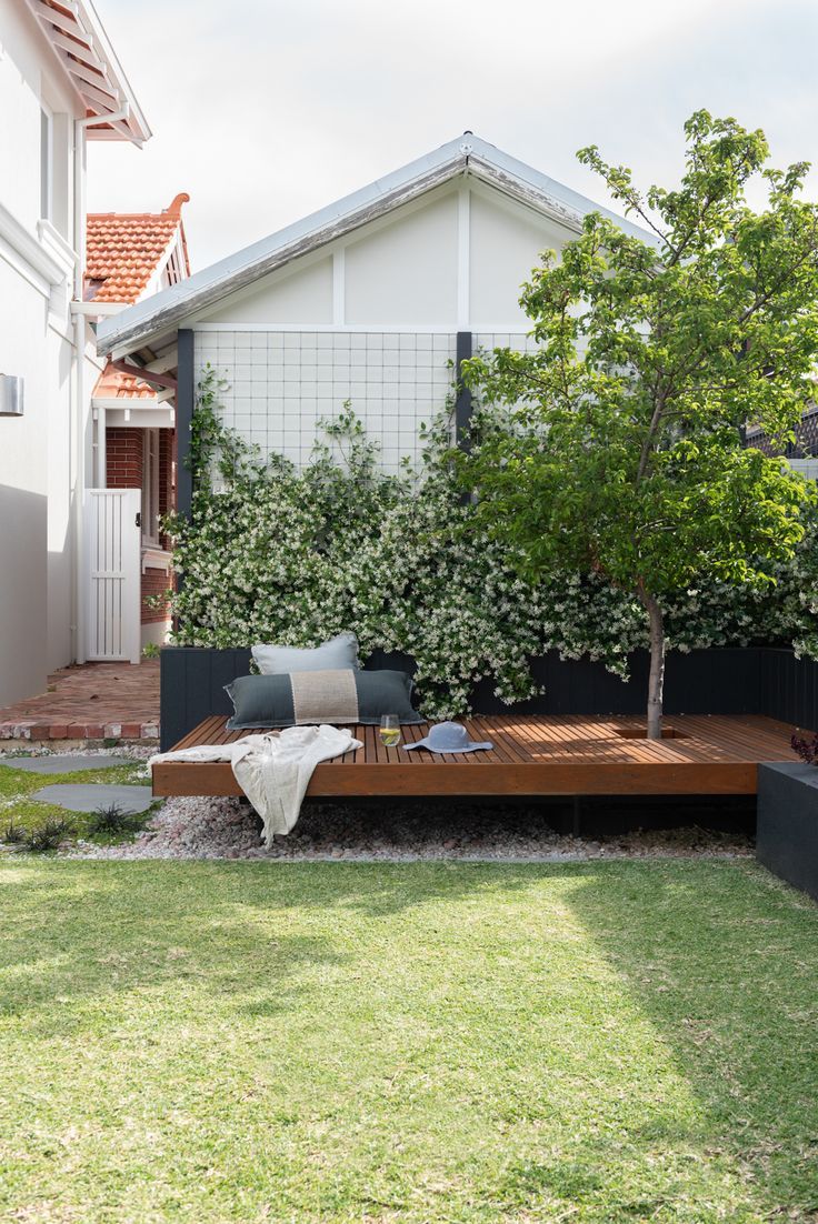 an outdoor living area with wooden decking and plants on the side of the house