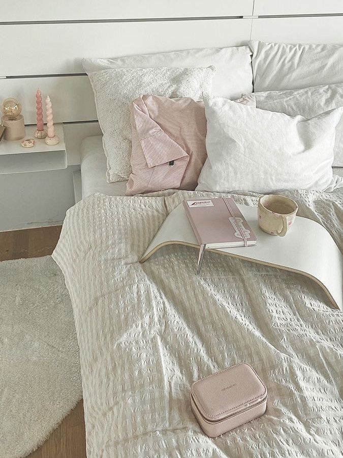 a white bed topped with pillows and blankets next to a night stand filled with books