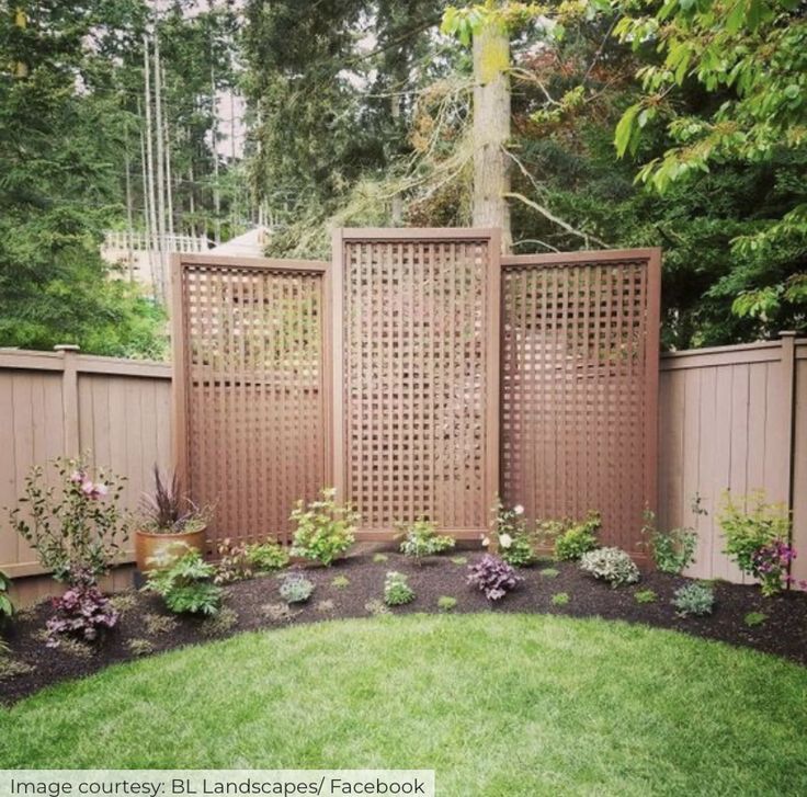 a backyard with a wooden fence and flowers in the center, surrounded by green grass