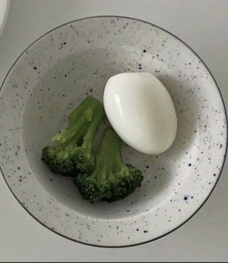 two pieces of broccoli and an egg in a white bowl on a table