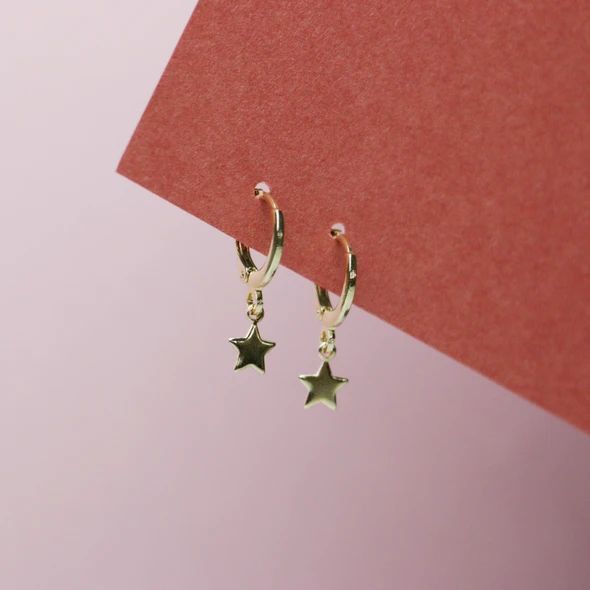 two small stars hanging from the side of a pair of hoop earrings on a pink background