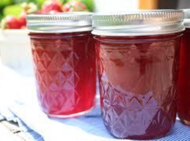 three jars filled with red liquid sitting on top of a blue table cloth next to strawberries