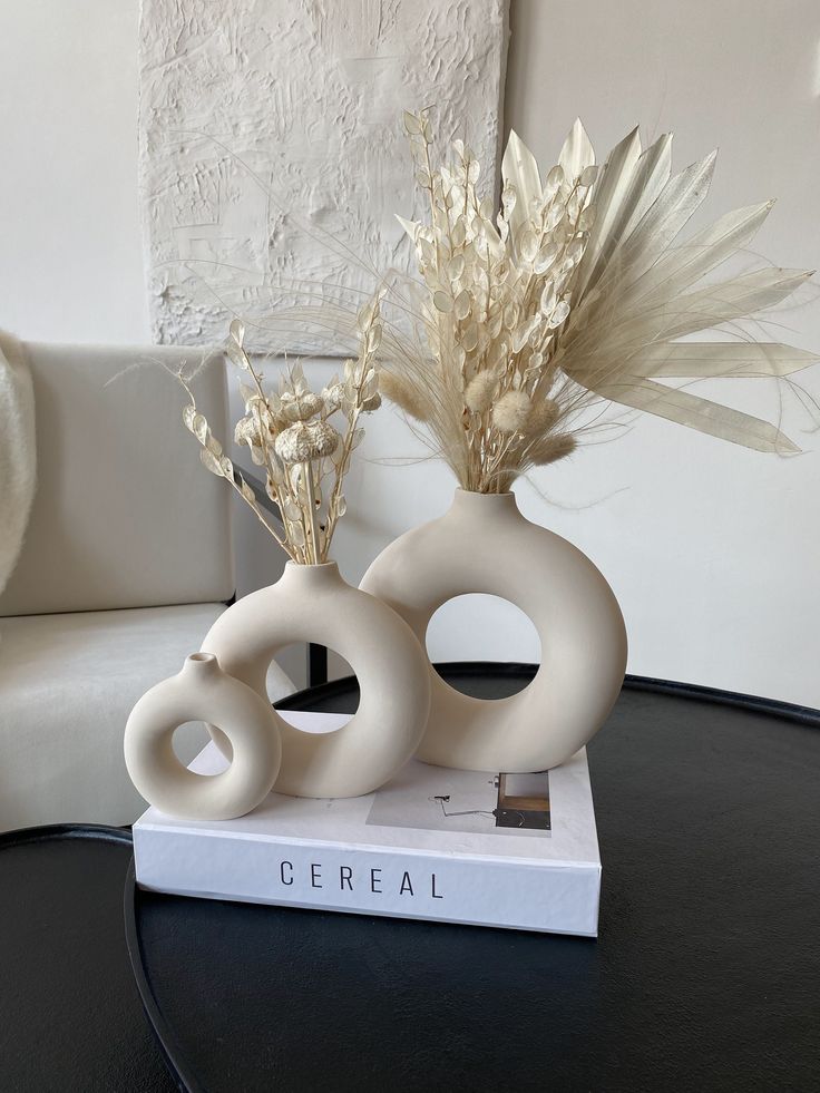 two white vases sitting on top of a table with dried flowers in each one