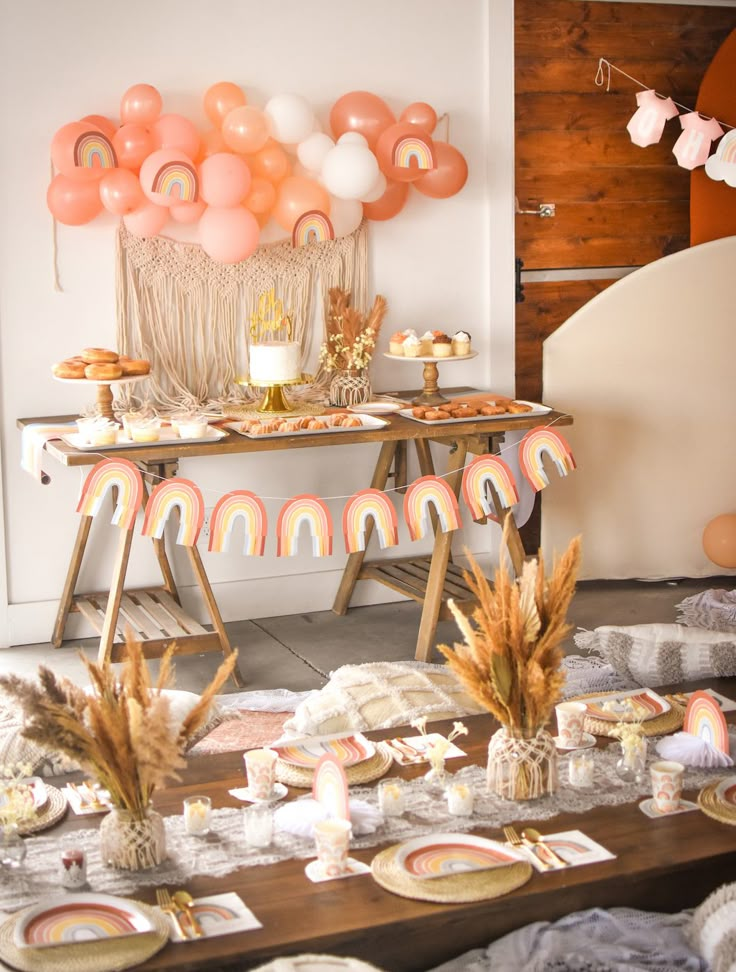 a table topped with lots of desserts next to a wooden table covered in balloons