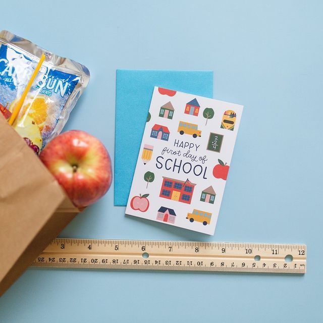 an apple next to a brown paper bag with school supplies on it and a ruler