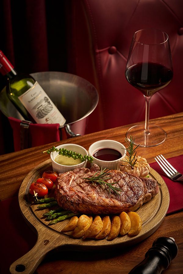 a plate with steak, asparagus and tomatoes next to a glass of wine