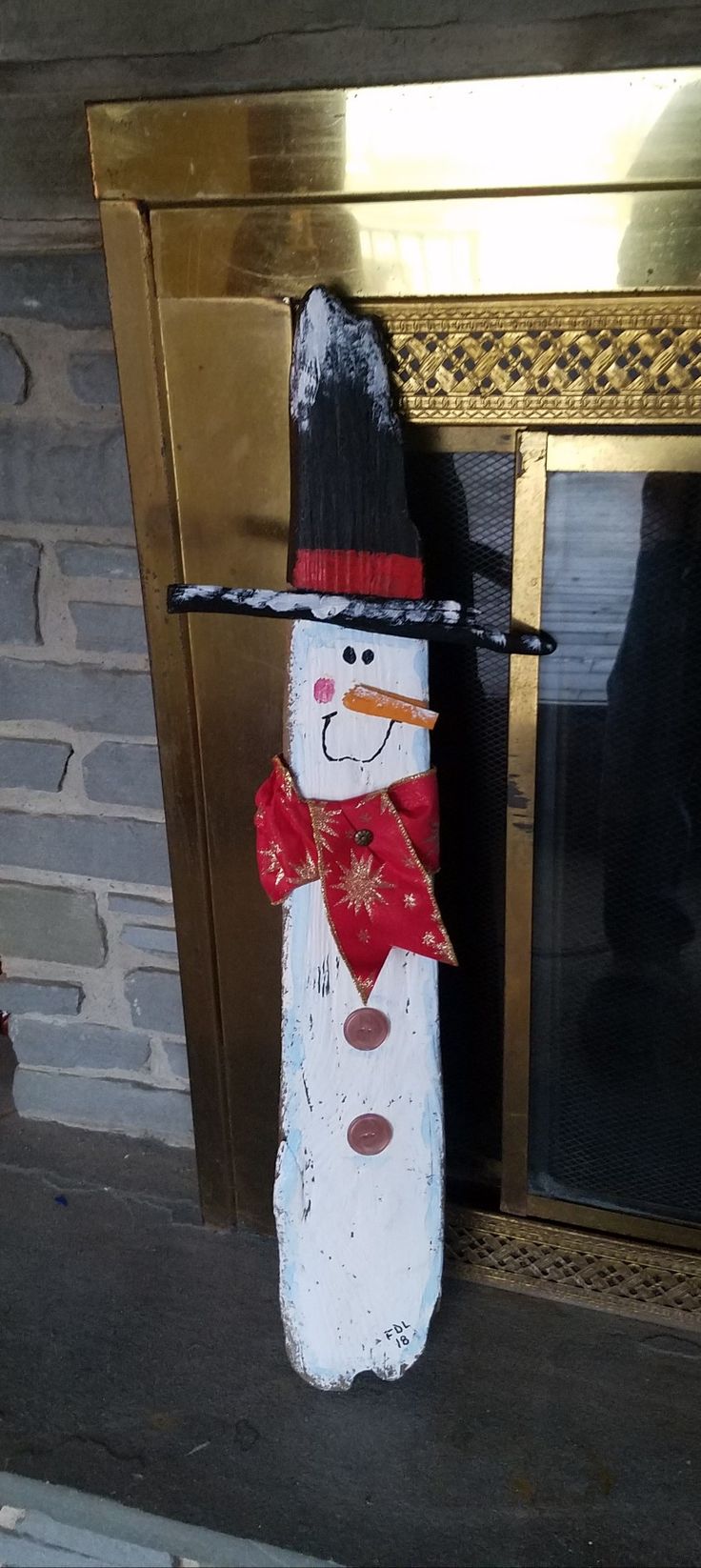 a wooden snowman with a black hat and red scarf standing in front of a fireplace