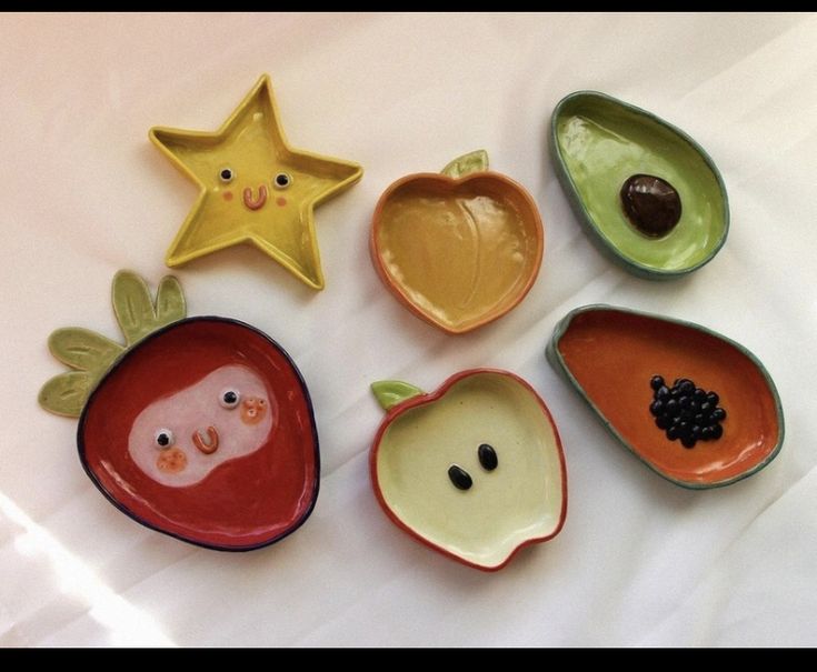 five ceramic fruits and vegetables are arranged on a white tablecloth with star shaped objects in the background