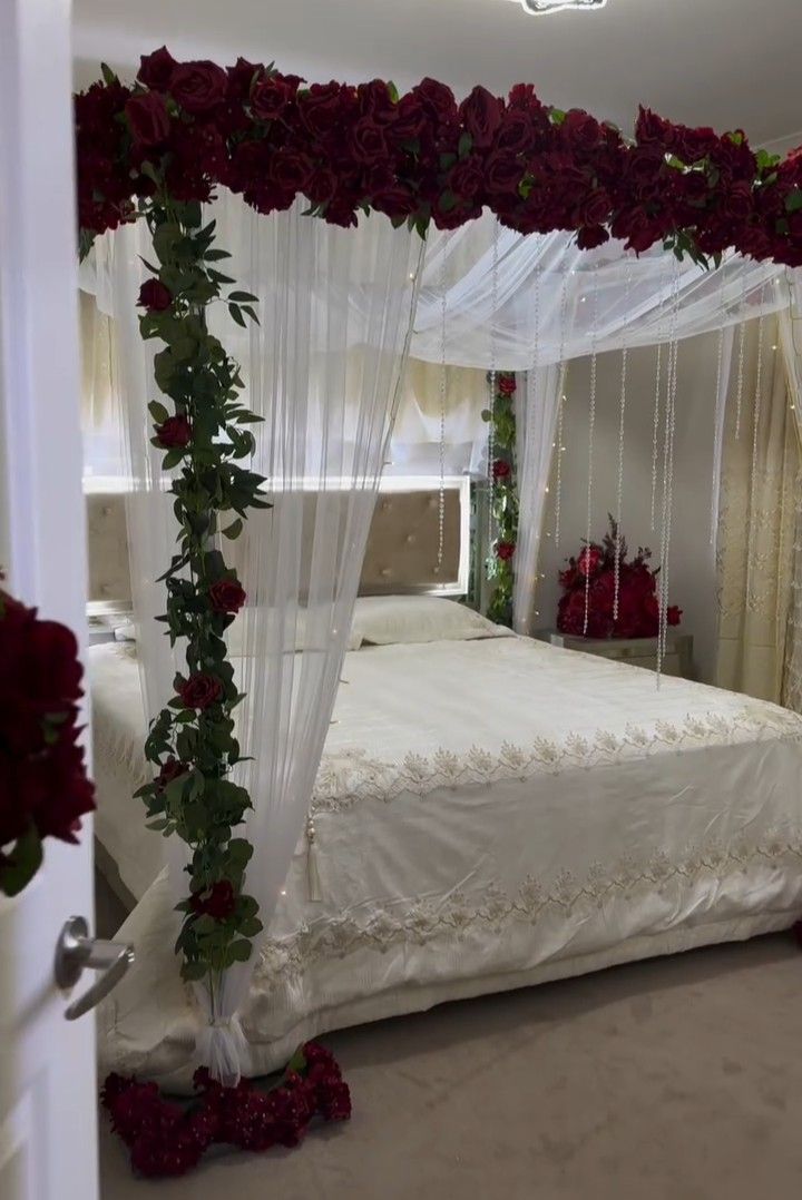 a bed with white sheets and red flowers on the headboard is decorated with greenery