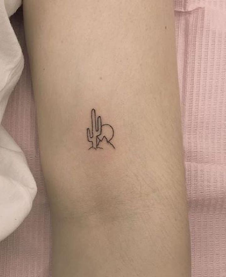 a small cactus tattoo on the left inner arm, with an arrow in the middle