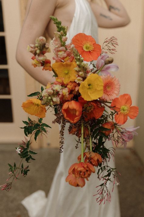 a woman in a white dress holding a bouquet of orange and yellow flowers on her wedding day